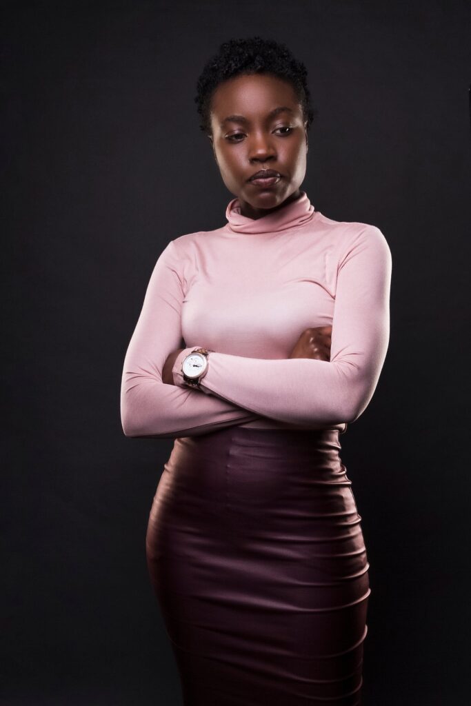 black woman wearing pink turtleneck and purple leather skirt with arms crossed.