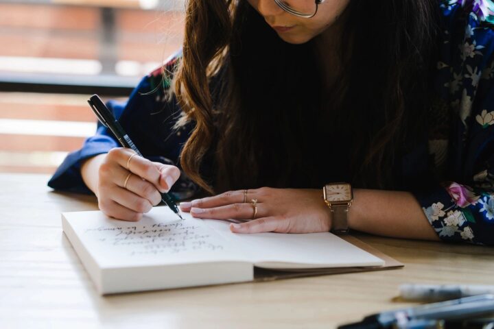 Person writing in notebook at wooden table