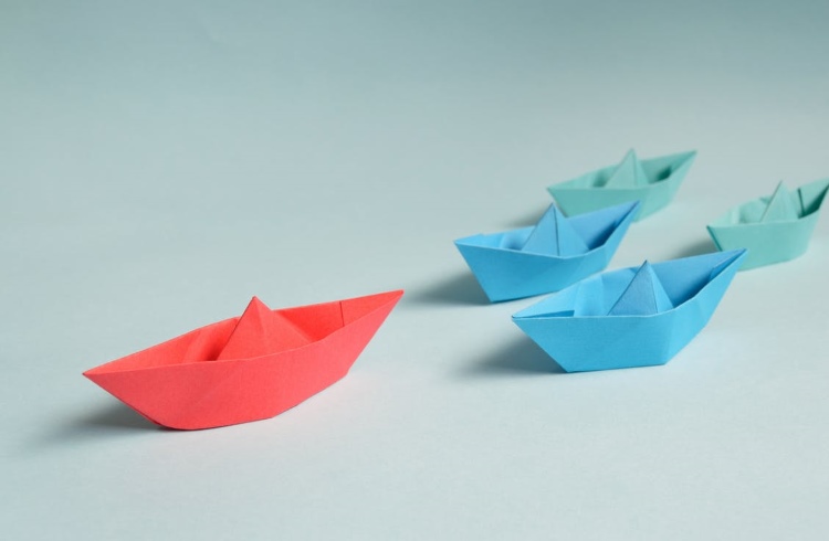 Red origami boat leading blue paper boats